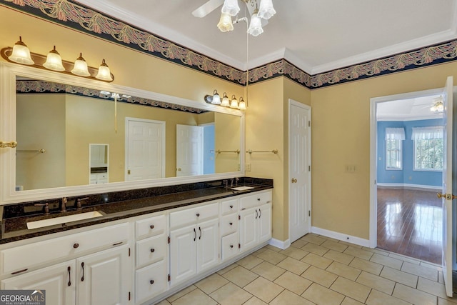 bathroom featuring a ceiling fan, baseboards, double vanity, ornamental molding, and a sink