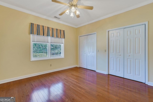 unfurnished bedroom featuring crown molding, wood finished floors, visible vents, and two closets