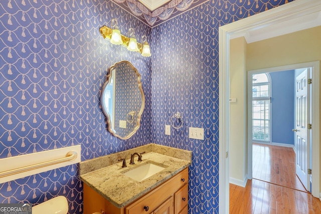 bathroom featuring ornamental molding, wood finished floors, wallpapered walls, baseboards, and vanity