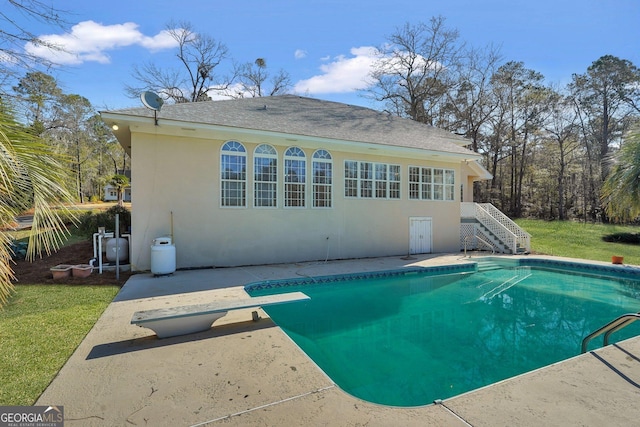 back of property featuring stucco siding, roof with shingles, an outdoor pool, stairs, and a patio area