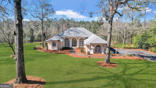 mediterranean / spanish home featuring a wooded view, stucco siding, driveway, and a front lawn