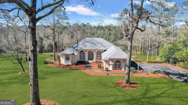 mediterranean / spanish-style home featuring aphalt driveway, a view of trees, a front lawn, and stucco siding