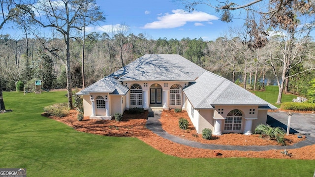 mediterranean / spanish-style house featuring stucco siding, a wooded view, and a front yard