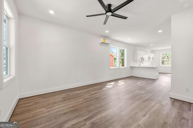 unfurnished living room with a wall mounted air conditioner, baseboards, wood finished floors, and recessed lighting