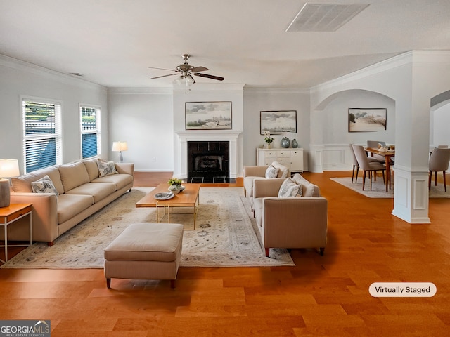 living area with visible vents, crown molding, ceiling fan, wood finished floors, and arched walkways