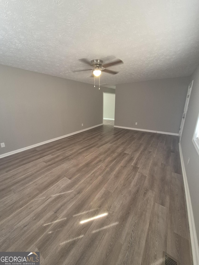 spare room with baseboards, dark wood-type flooring, a ceiling fan, and a textured ceiling