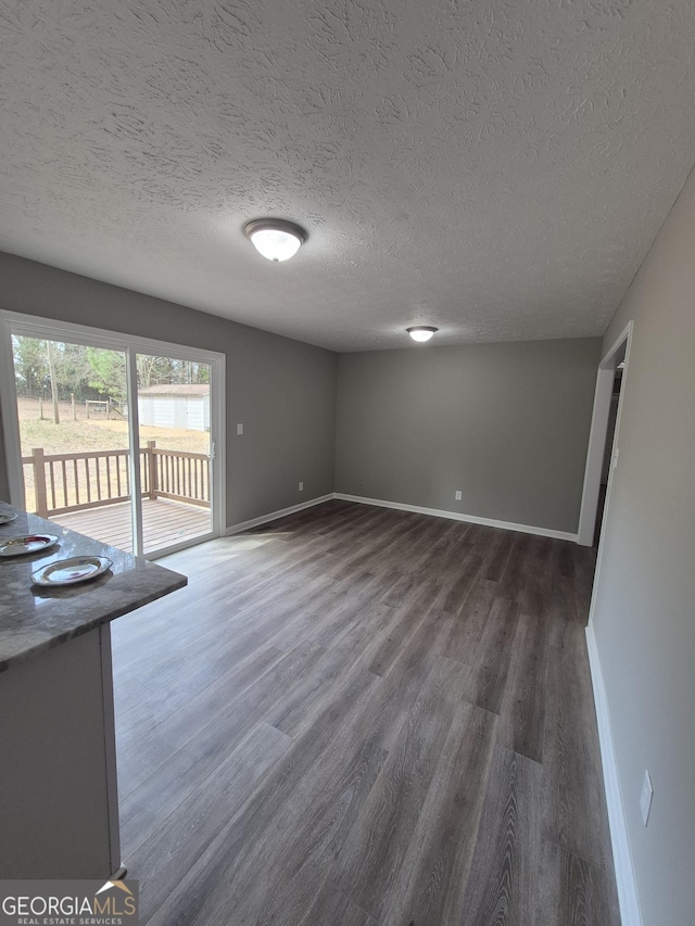 unfurnished living room featuring dark wood finished floors, baseboards, and a textured ceiling