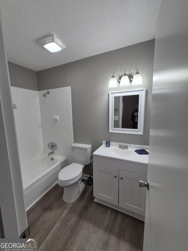 bathroom with toilet, a textured ceiling, wood finished floors, bathing tub / shower combination, and vanity