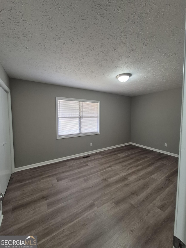 spare room featuring dark wood finished floors, visible vents, baseboards, and a textured ceiling