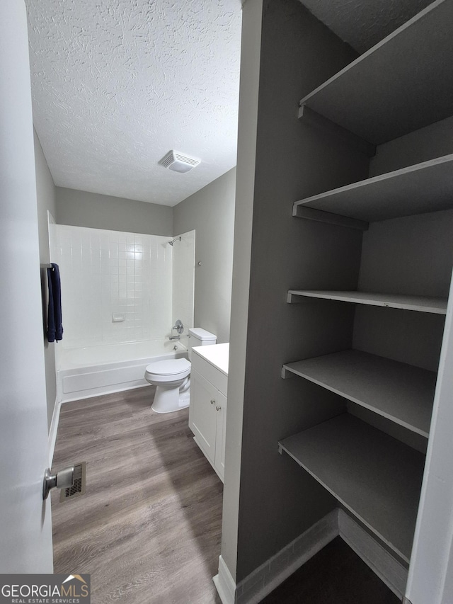 bathroom with toilet, vanity, wood finished floors, a textured ceiling, and  shower combination