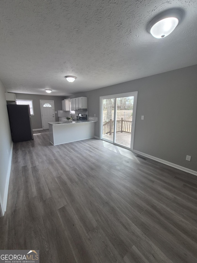 unfurnished living room featuring a textured ceiling, dark wood-type flooring, and baseboards