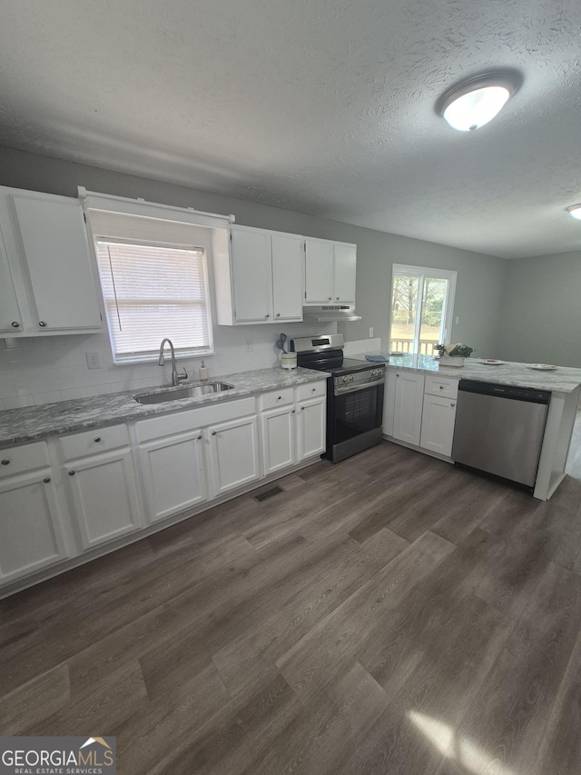 kitchen featuring dark wood finished floors, a peninsula, a sink, stainless steel appliances, and white cabinetry