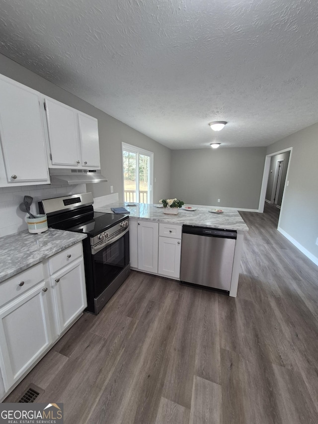 kitchen with under cabinet range hood, dark wood finished floors, white cabinetry, appliances with stainless steel finishes, and a peninsula