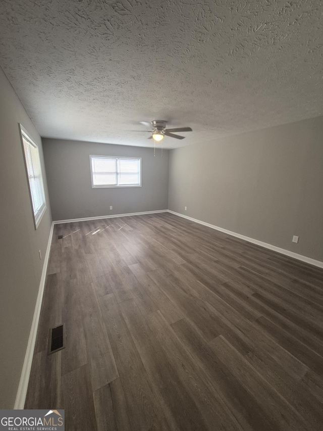 empty room featuring a ceiling fan, visible vents, dark wood-style flooring, and baseboards