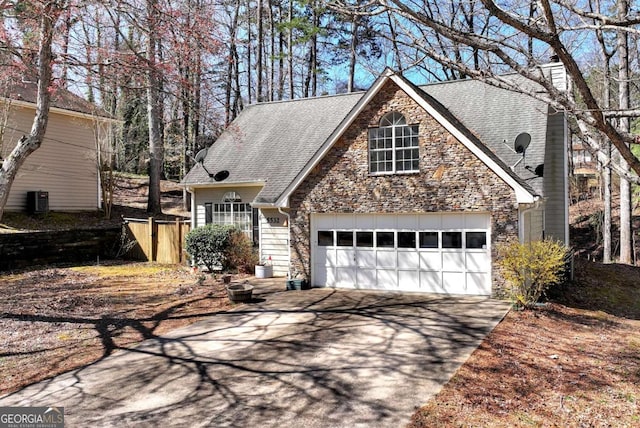 traditional-style house with central air condition unit, aphalt driveway, stone siding, a shingled roof, and a garage