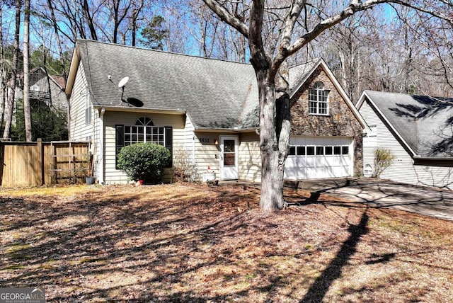 view of front facade with fence, a shingled roof, concrete driveway, a garage, and stone siding