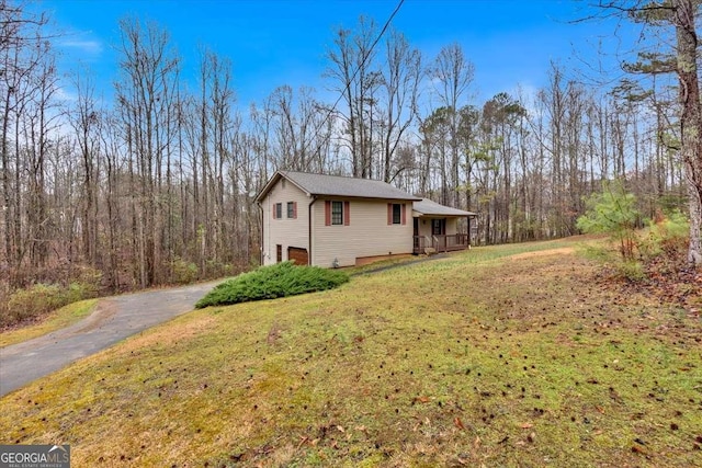 view of side of property with aphalt driveway, a forest view, and a yard