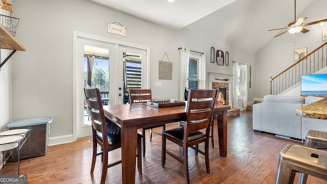 dining room featuring stairway, a fireplace, french doors, wood finished floors, and a ceiling fan