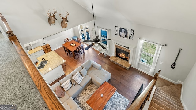 living area with baseboards, a stone fireplace, wood finished floors, and a ceiling fan