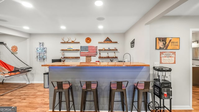 bar with baseboards, recessed lighting, a sink, indoor wet bar, and light wood-type flooring