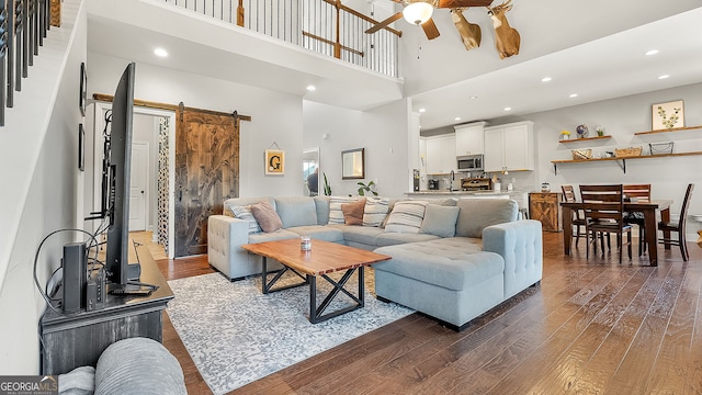 living area featuring dark wood finished floors, recessed lighting, ceiling fan, a towering ceiling, and a barn door