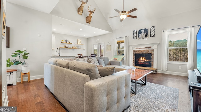 living room featuring a wealth of natural light, a stone fireplace, dark wood-type flooring, and baseboards