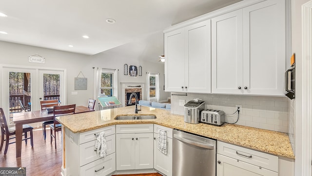 kitchen with a sink, a peninsula, white cabinets, decorative backsplash, and dishwasher