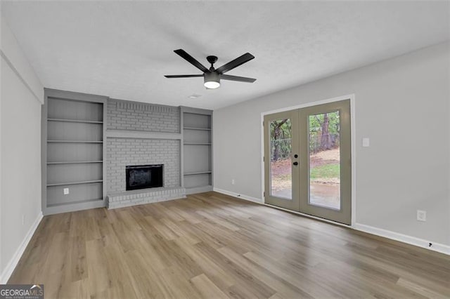 unfurnished living room featuring built in features, a brick fireplace, light wood-type flooring, and baseboards