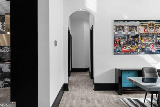 corridor with arched walkways, baseboards, and wood finished floors