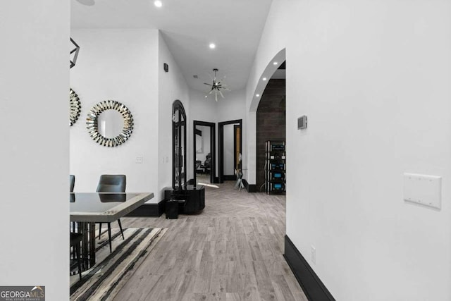 corridor featuring arched walkways, recessed lighting, baseboards, and wood finished floors