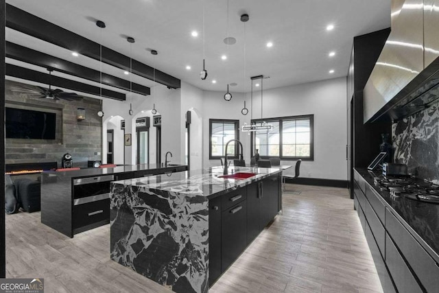 kitchen with a large fireplace, a large island, dark cabinetry, arched walkways, and a sink