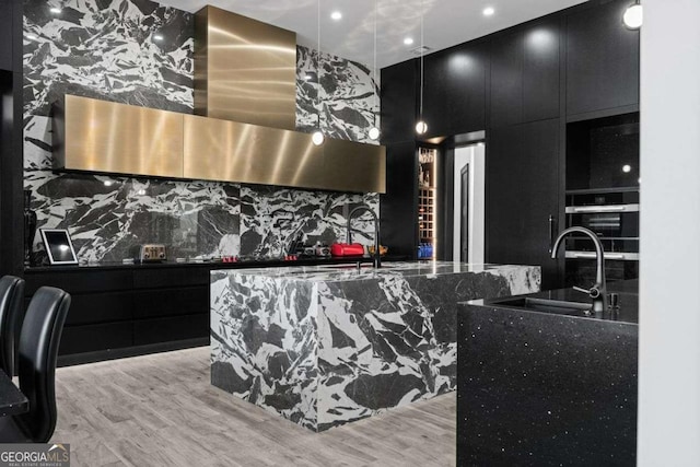 kitchen featuring light wood finished floors, modern cabinets, dark cabinetry, and wall chimney range hood