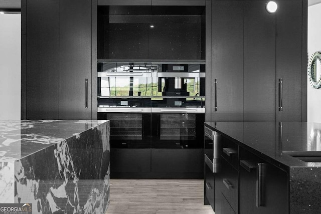 kitchen featuring light wood finished floors, dark stone countertops, modern cabinets, and dark cabinetry