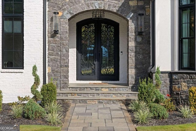 view of exterior entry with brick siding, stone siding, and french doors