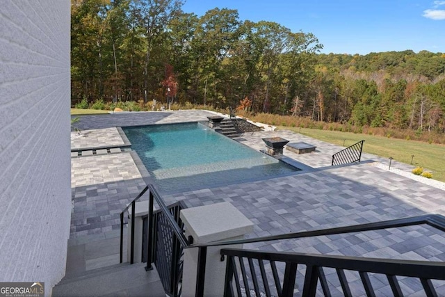 view of pool with a patio, a view of trees, and an infinity pool