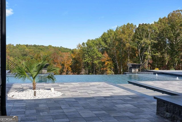 view of swimming pool with a forest view, an infinity pool, and a patio