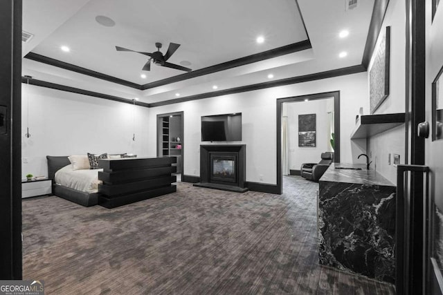 carpeted bedroom with crown molding, baseboards, a glass covered fireplace, a raised ceiling, and a sink