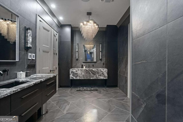 bathroom with visible vents, two vanities, a sink, tile walls, and an inviting chandelier