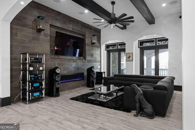 living room with beam ceiling, a fireplace, wood finished floors, arched walkways, and a ceiling fan