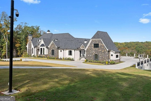 view of front of house featuring a front lawn, curved driveway, stone siding, and a chimney