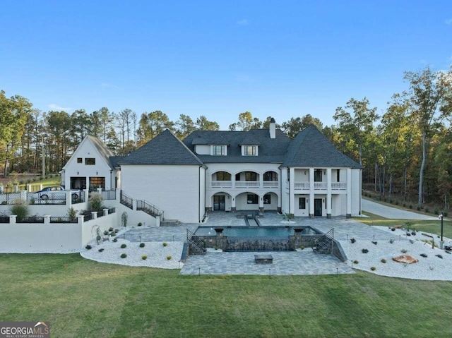 rear view of property with a patio, a balcony, a chimney, stairs, and a lawn