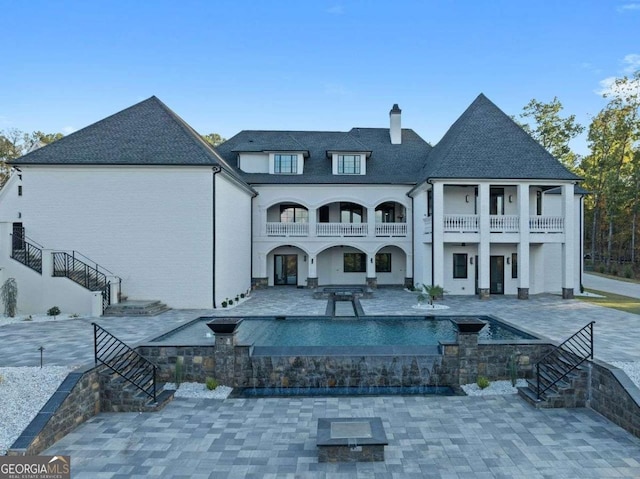 back of property featuring a balcony, stairway, an outdoor pool, a chimney, and a patio area