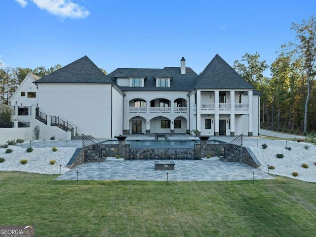 rear view of property featuring stairway, a chimney, a yard, a balcony, and a patio area