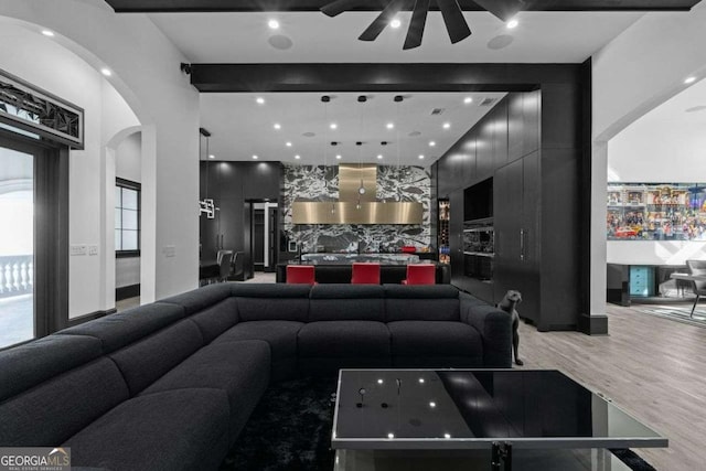 living area with arched walkways, light wood finished floors, and a ceiling fan