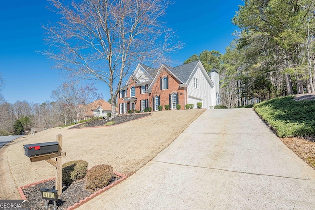 traditional-style house featuring brick siding, a chimney, and driveway