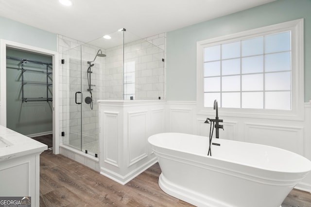 full bathroom with wood finished floors, wainscoting, a stall shower, a freestanding tub, and vanity