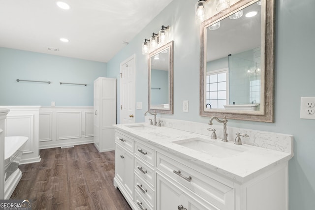 full bathroom with double vanity, a wainscoted wall, wood finished floors, and a sink