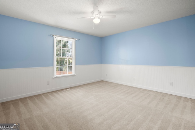 spare room featuring a wainscoted wall, a textured ceiling, carpet, and a ceiling fan