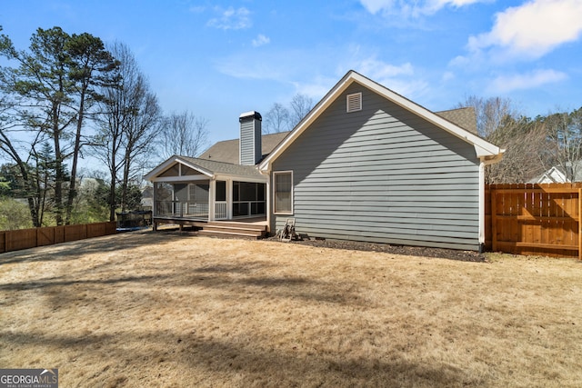 rear view of house featuring a shingled roof, a fenced backyard, a chimney, and a sunroom