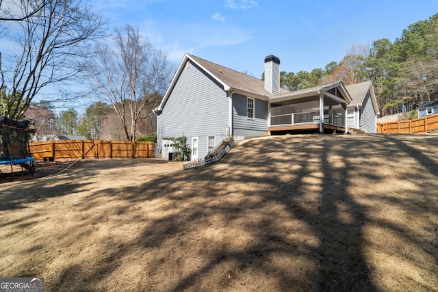 rear view of house featuring a trampoline, a fenced backyard, an attached garage, and a chimney